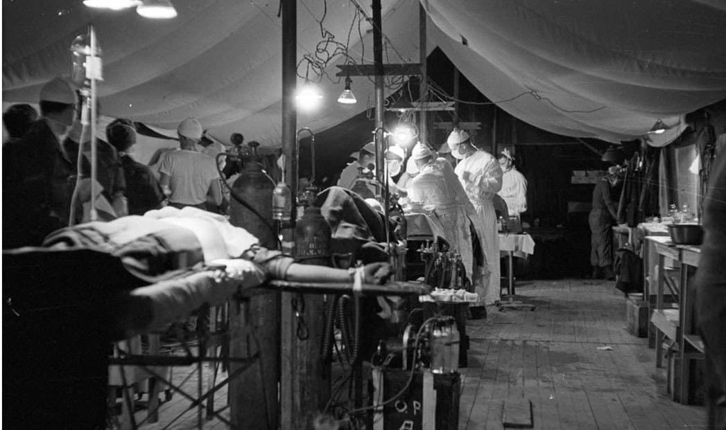 Surgeons operating inside a canvas field hospital tent
